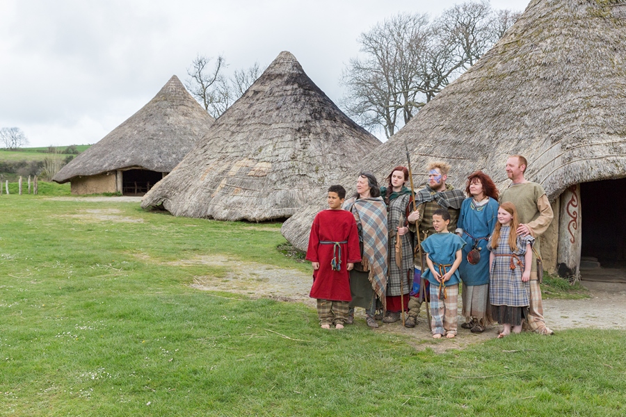 A family of seven standing outside three roundhouses at Castell Henllys