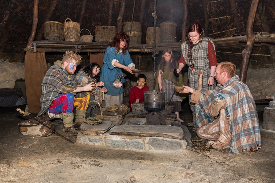 Seven members of an Iron Age family sit round the fire in an Iron Age roundhouse at Castell Henllys