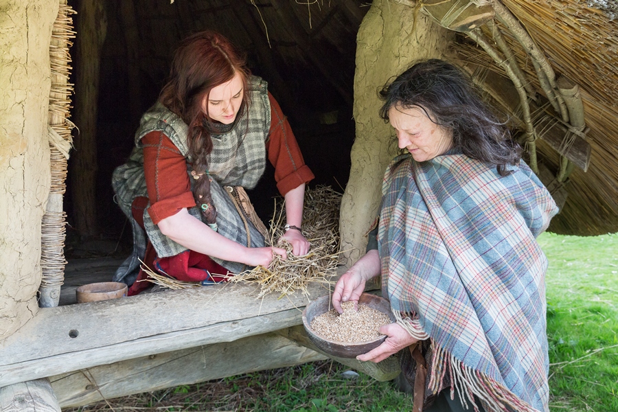 Two women with bowl of grain at door of roundhouse