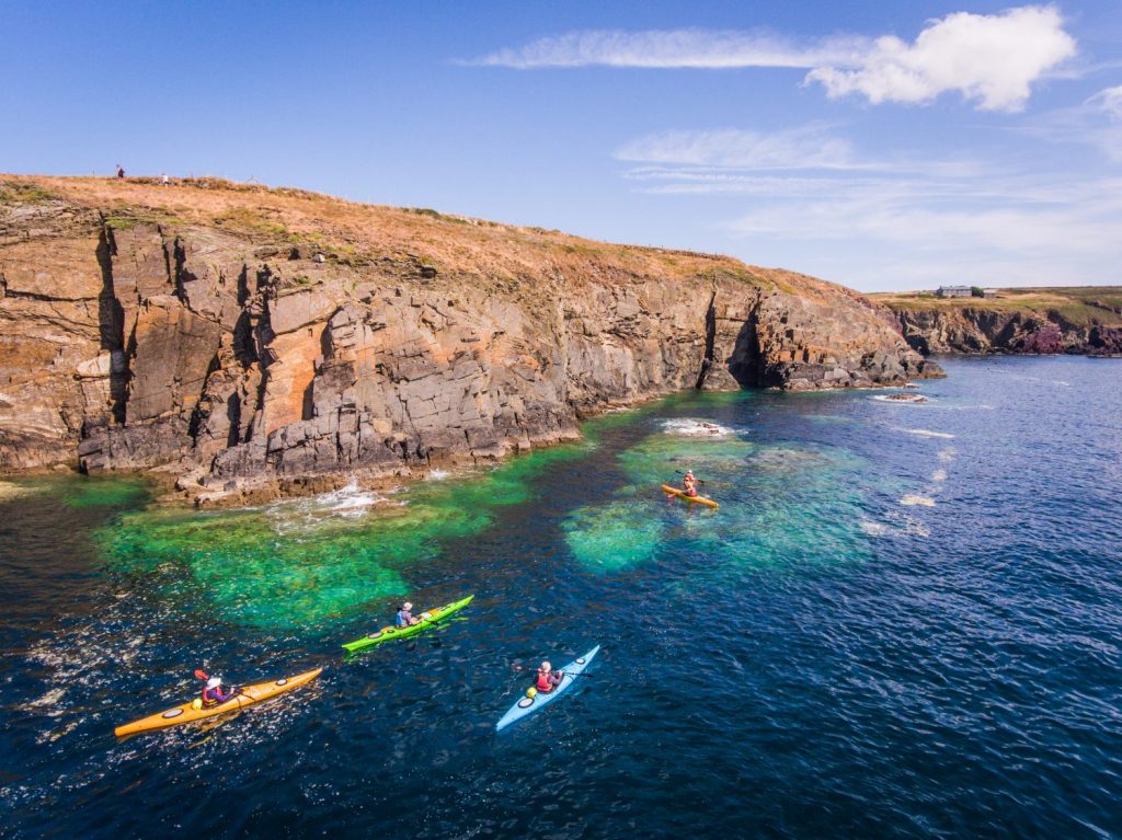 People walking on the Coast Path and kayaking at Porth Clais near St Davids, Pembrokeshire Coast National Park, Wales, UK