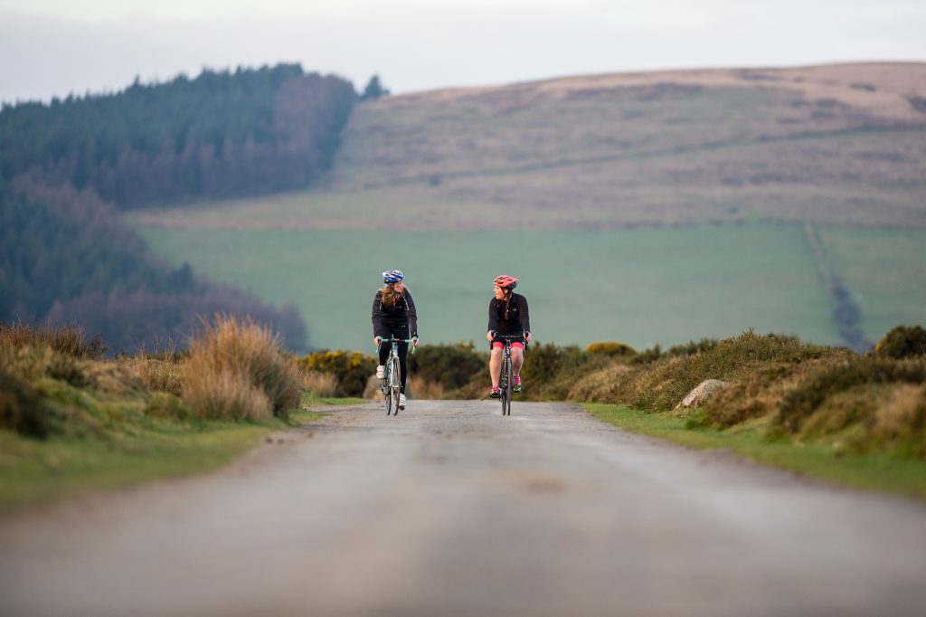 Two women cycling on a narrow road