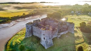 A ruined stone castle next to a river viewed from the air