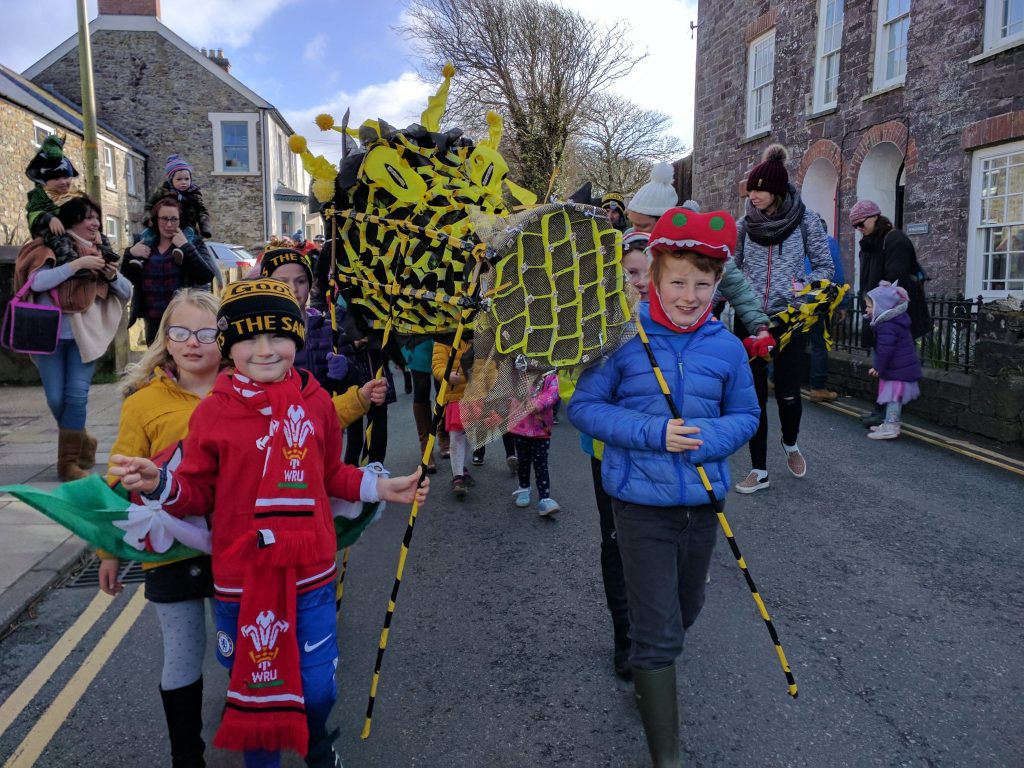 Group of children parading through a street holding a dragon sculpture