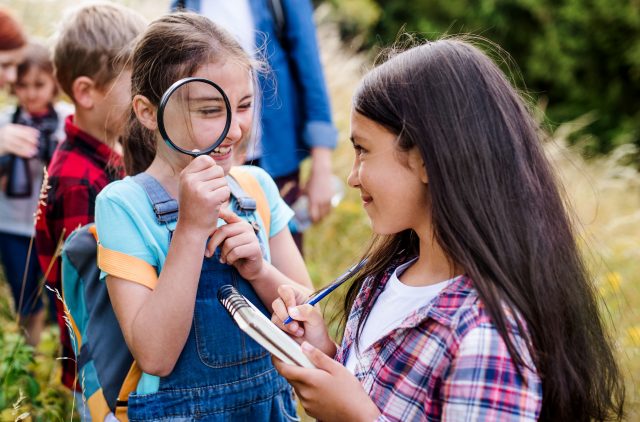 A group of small school children with teacher on field trip in nature, learning science.