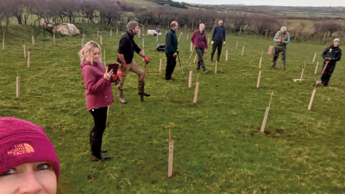 Group of people standing in a field next to newly planted trees