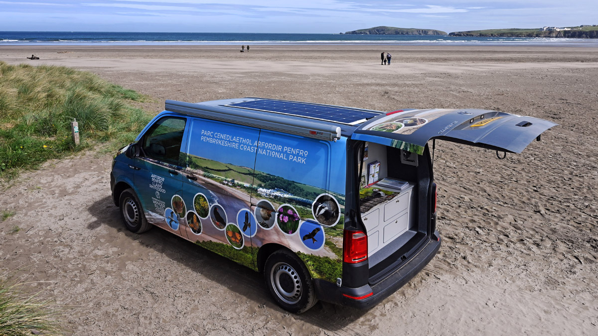 Camper van parked at the edge of a sandy beach. Beach pictured is Poppit Sands, Pembrokeshire, Wales, UK
