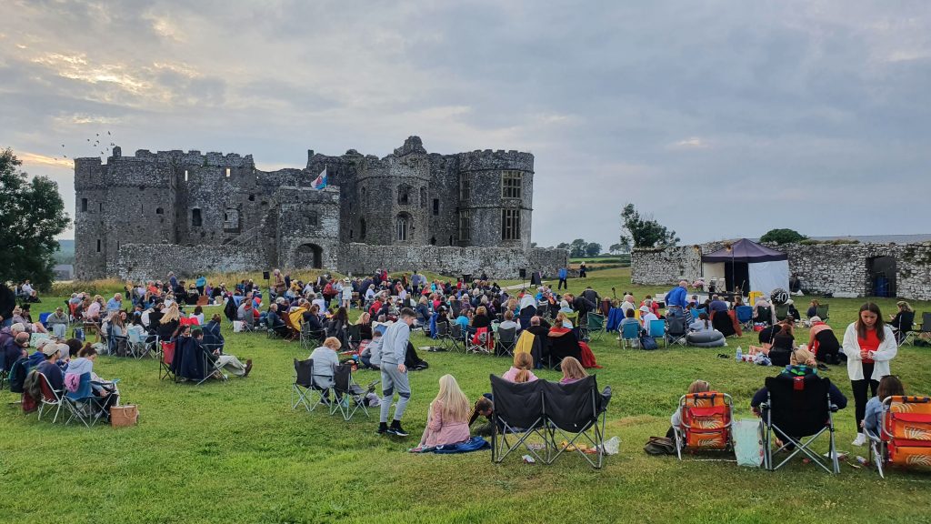 People seated on the grass outside a stone Castle - Castle pictured is Carew Castle