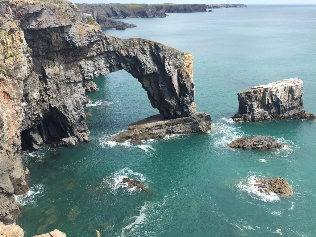 Limestone sea arch reaching from the mainland into the sea with aqua marine seas below. Location pictured is the Green Bridge of Wales, Pembrokeshire