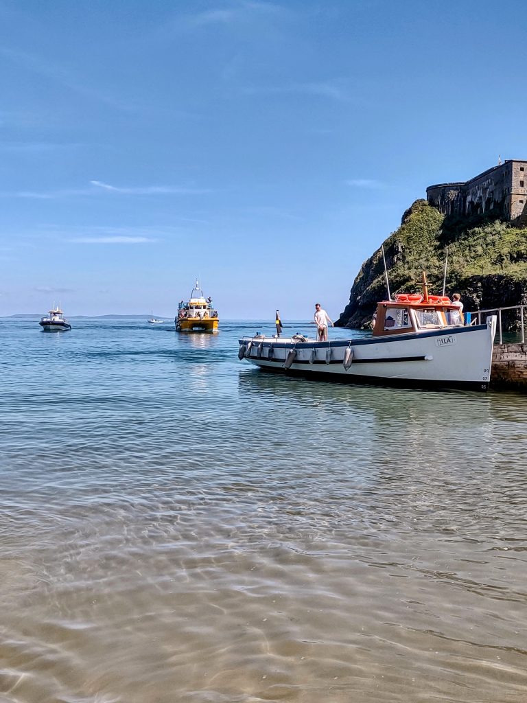 Boat moored next to an island in shallow water with two further boats approaching. Location pictured is Tenby, Pembrokeshire