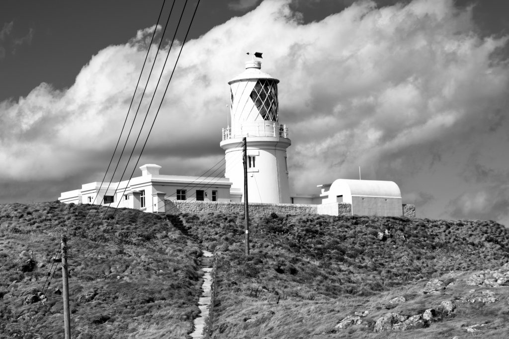Black and white photograph of a lighthouse atop a grassy hill. Location photograph is Strumble Head