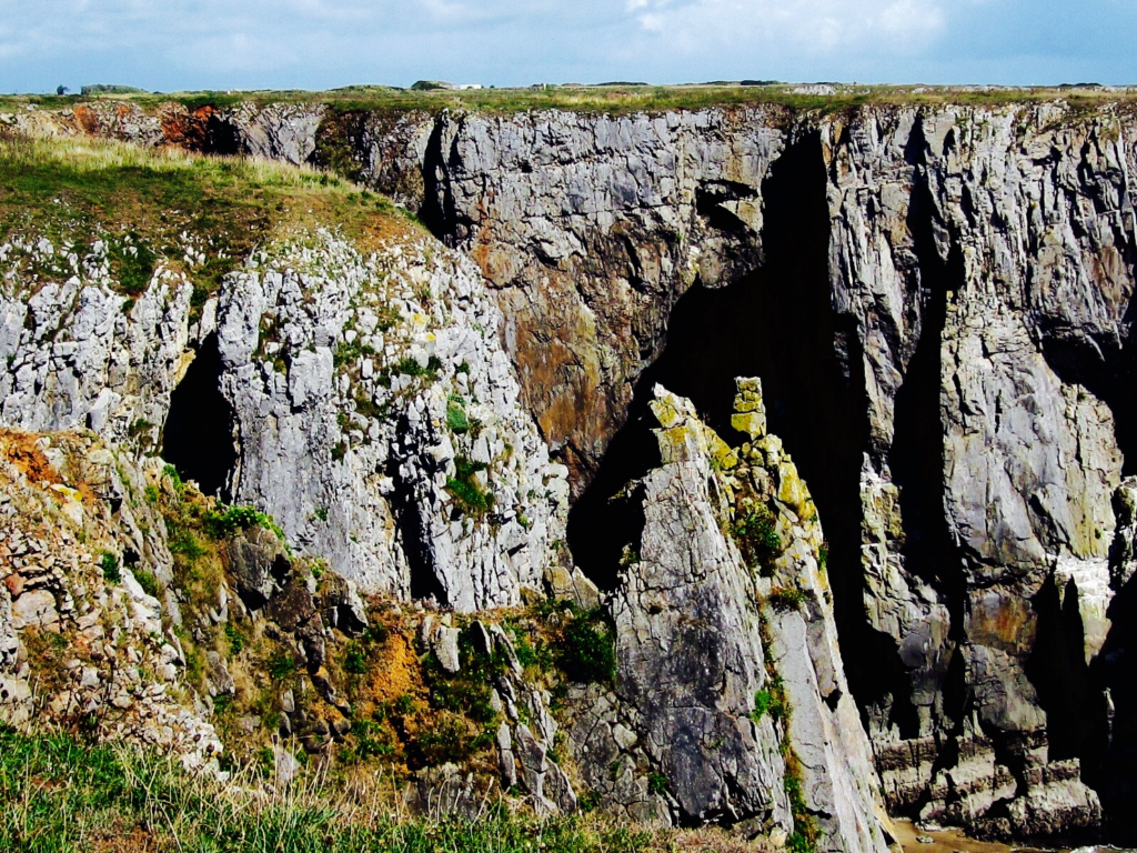 Limestone cliffs topped with green and yellow grass with blue skies above. Location is Stack Rocks, Pembrokeshire