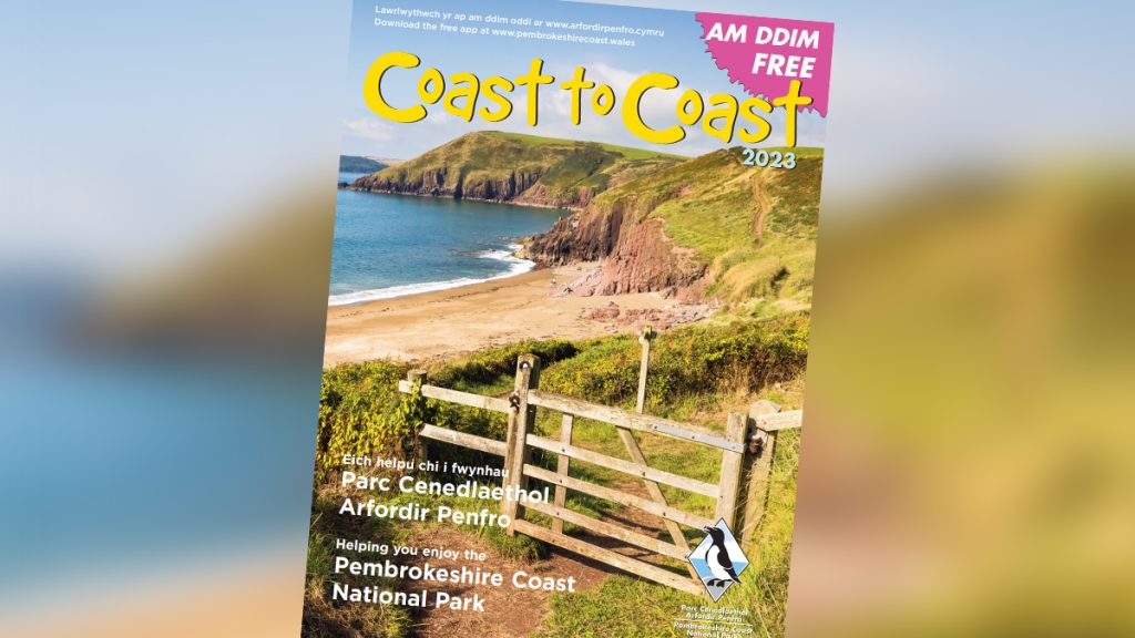 Cover of a magazine titled 'Coast to Coast' which features a coastal scene including a wooden gate across a footpath leading to a sandy beach with red sandstone cliffs in the distance.