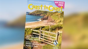 Cover of a magazine titled 'Coast to Coast' which features a coastal scene including a wooden gate across a footpath leading to a sandy beach with red sandstone cliffs in the distance.