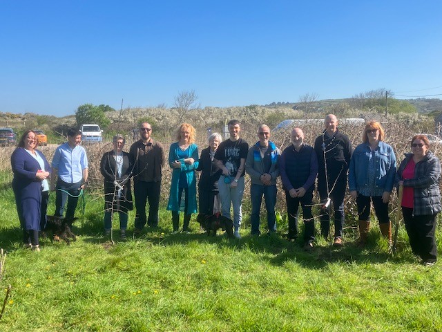 Group of people standing on a grassy verge alongside newly planted trees. Location pictured is Poppit Sands, Pembrokeshire