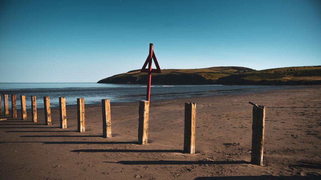 Empty sandy beach with wooden fence posts dotted along the shore on a sunny day. Location in picture is Newport Sands, Pembrokeshire