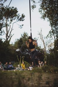 A circus performer hangs through a suspended hoop in front of an audience