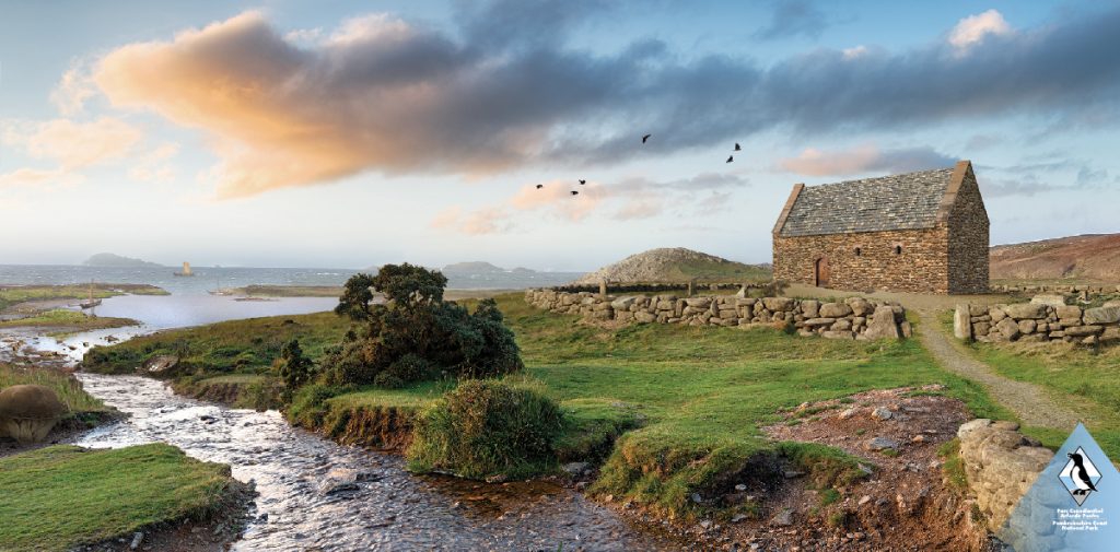 3d reconstruction of a stone chapel building set in a grassy field next to a river running down to the sea. Location is St Patrick's chapel, Whitesands Bay, St Davids, Pembrokeshire