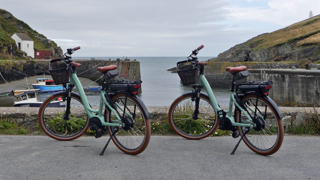 Two e-bikes leaning on their kick stands at the edge of a harbour wall. Location pictured is Porthgain, Pembrokeshire