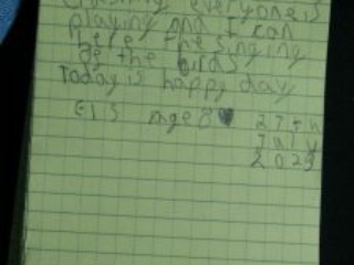 Poem written in a notebook. It reads: Today the sea is crashing everyone is playing and I can ear the singing of the birds. Today is a happy day. Eis age 8. 27th July 2023.