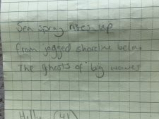 Poem written in a notebook. It reads: Sea spray rises up From jagged shoreline below The ghosts of big waves  Hilly (41) Bethan