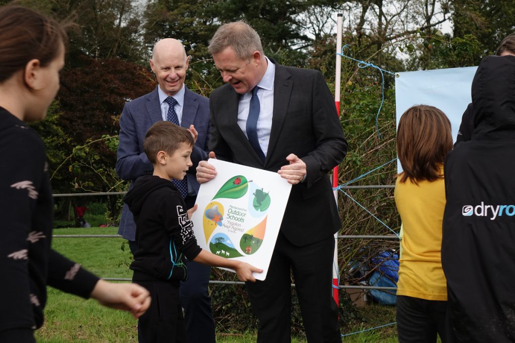 Welsh Government Minister for Education and the Welsh Language, Jeremy Miles MS presenting a Pembrokeshire Outdoor Schools plaque to pupils of a school to recognise their commitment to outdoor learning. (