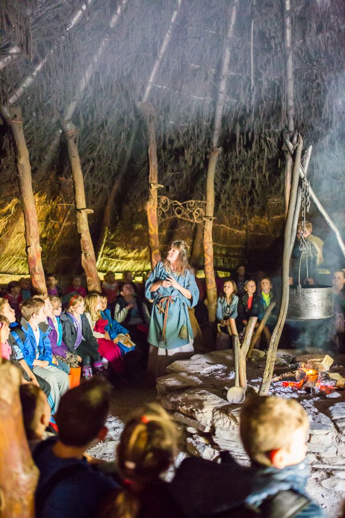 School children gathered around the fire in one of Castell Henllys' roundhouses, listening to a costumed guide.