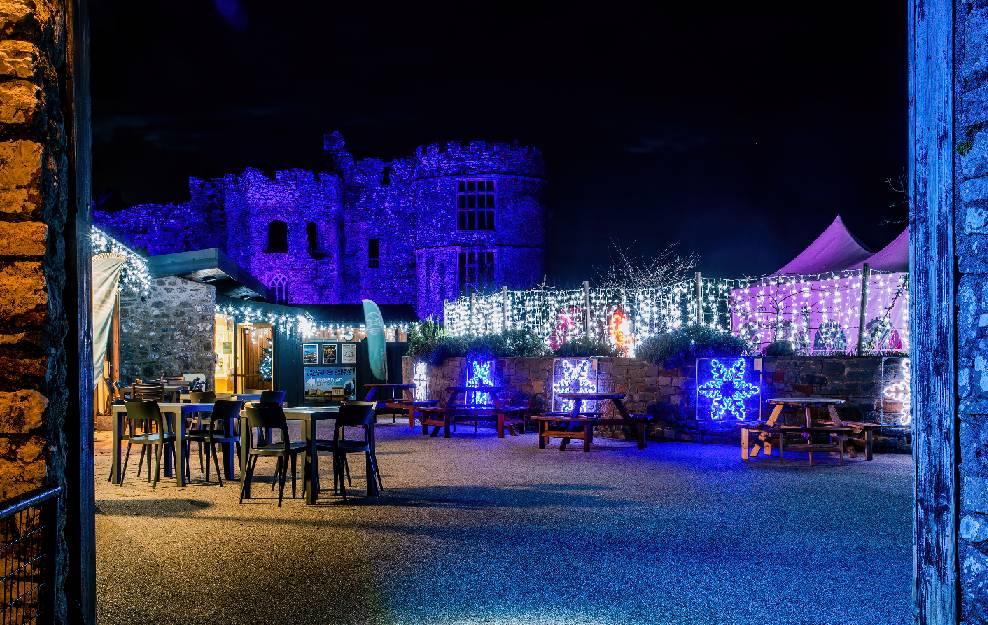 Carew Castle's Walled Garden illuminated, with the Castle behind it.