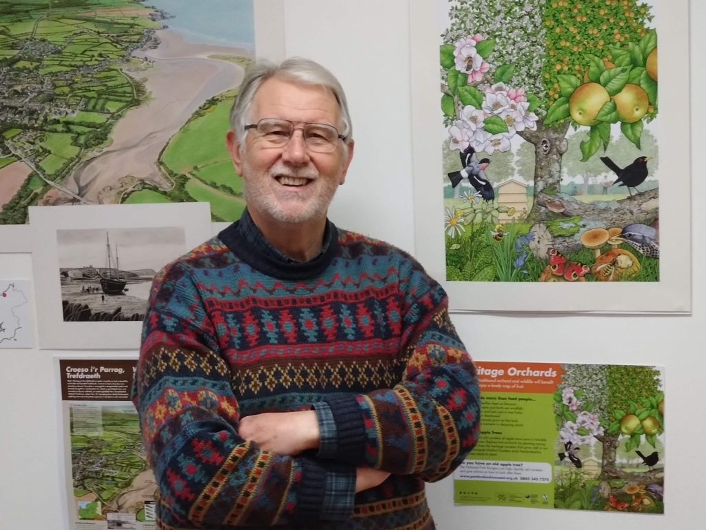 A photo of artist/illustrator Graham Brace standing in front of some of his illustrations