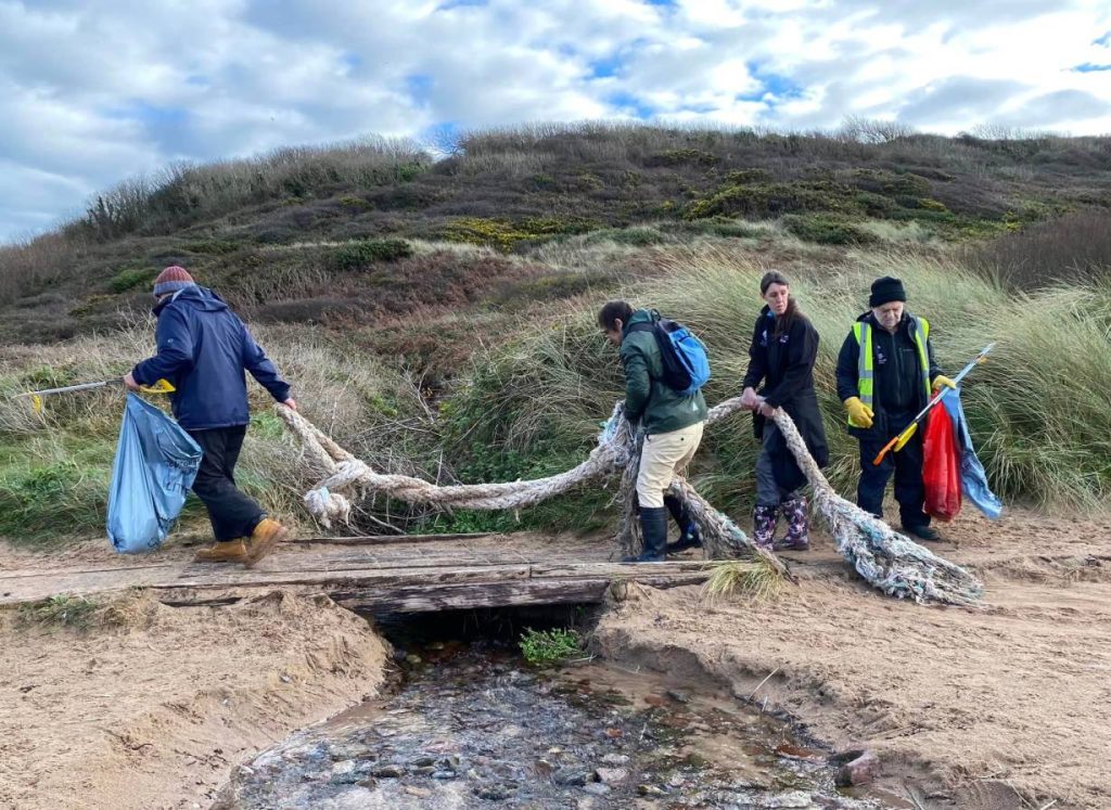 Four members of Roots to Recovery carrying a large discarded rope across a beach.