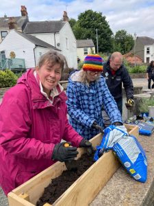 Three members of the Roots to Recovery group filling planters with soil.