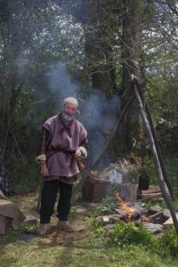 An Iron Age Villager from Castell Henllys in front of an open fire.