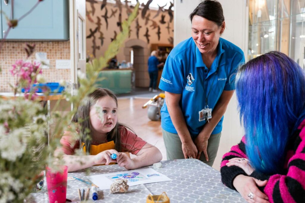 A little girl taking part in some creative craft work with an assistant on hand